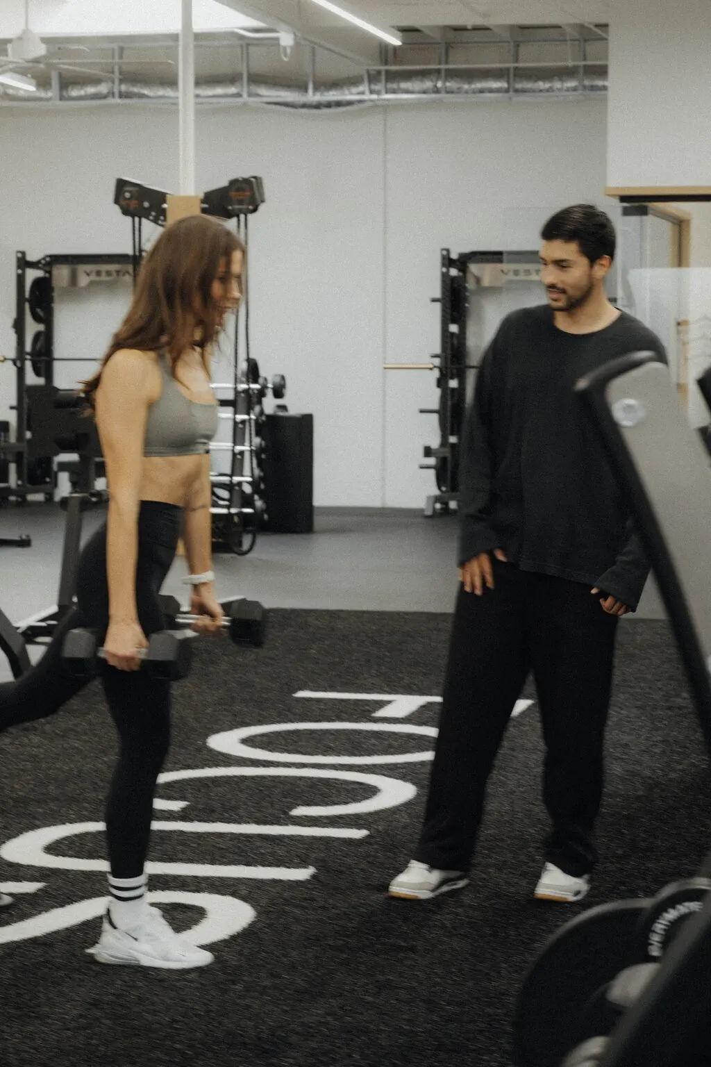 A client deadlifting dumbbells on the FOCUS turf while Coach Santi coaches nearby, personal training on the gym floor at Focus Athletics in Costa Mesa